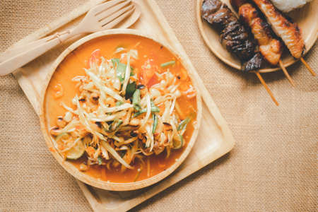 Green papaya salad Thai cuisine spicy delicious called SOM-TAM on wood dish, eating with sticky rice, grilled chicken and grilled liver. Spicy thai food.の写真素材