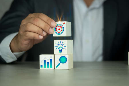 Businessman arranging wood block with target icon and business icon for strategy, action plan, growth business ,success process concept.の写真素材