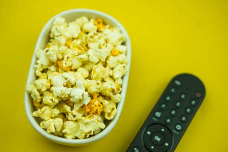 A bowl of popcorn and remote control. Minimal concept of cable or digital television. Family watching TV shows together. Selective focusの写真素材