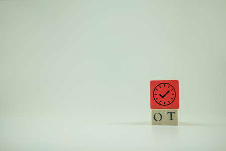The abbreviation OT on wooden cubes and clock icon. OT acronym over time, refers to hours worked that exceed their normally scheduled working hours.の写真素材
