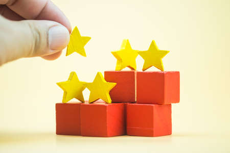 The customer hand putting wooden yellow star symbol shape to complete five star, evaluation, increase rating, customer experience, satisfaction and best excellent services rating concepts.の写真素材