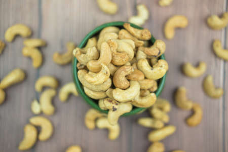 Green bowl with cashew nuts on wooden table. Top view and selective focus