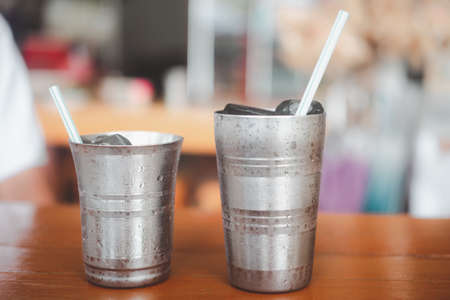 Water with ice in a metal glass on a wooden table at a local Thai restaurantの写真素材