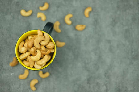 Yellow ceramic cup filled with cashew nuts spilled around. Selective focusの写真素材