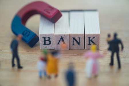 BANK word is written on wood block with blur foreground of miniature people. Banking saving...
