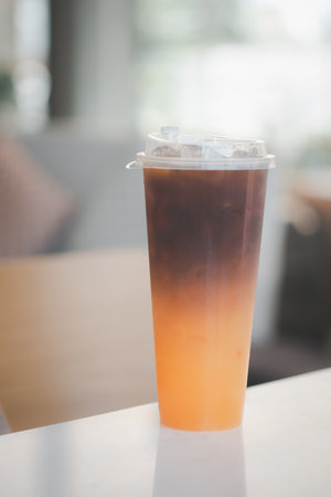 Cold iced black brew coffee mixed orange juice in a glass with pieces of ice on table, natural light, fresh summer drink in the morningの写真素材