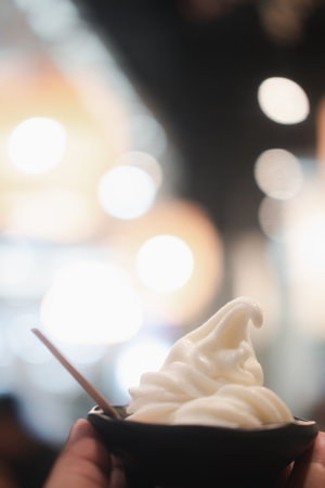 Soft serve vanilla ice cream in mini black bowl on hand with bokeh background