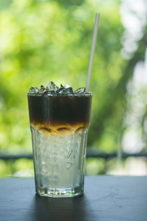 Americano coffee mixed with cool water in a clear glass can be seen in layers. Behind it is a...