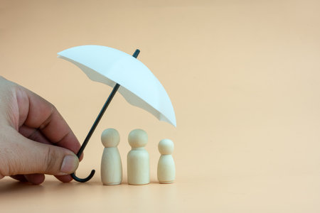White umbrella with wooden family peg dolls for protection with copy space. Family protection and insurance coverage concept. The insurance agent presents protection model that symbolize the coverage.の写真素材