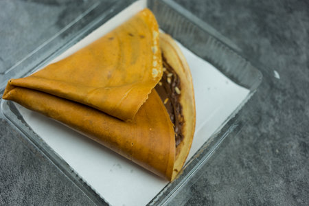 Crispy crepe pancake recipe by spreading crepe flour on hot stove into thin layer then filled chosen topping such as chocolate paste and cashew nuts served in boxの写真素材