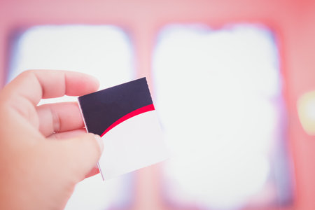 Hand holding a paper ticket on blurred cinema complex background (booking ticket concept)