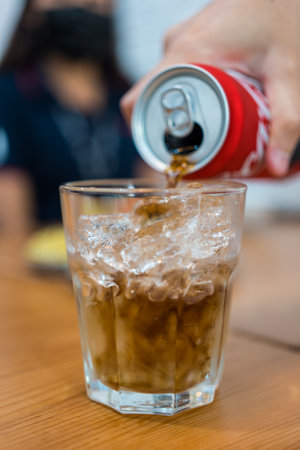 Bangkok, Thailand - December 25, 2022 : Pour the Coca-Cola soda drink from the can to the glass with ice. The beverage is produced and produced by Coca-Cola Company.のeditorial素材