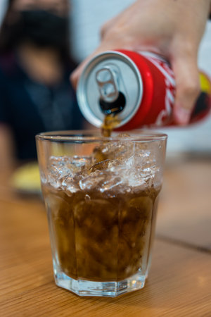 Bangkok, Thailand - December 30, 2022 : Cola can pouring in a glass with ice. The beverage is produced and produced by Coca-Cola Company.のeditorial素材