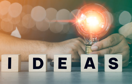 Hand holding light bulb with word Ideas on wood block. Ideas of new ideas with innovative and creativity. Development and promotion of creative ideas in businessの写真素材