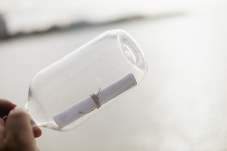 Bottle with a note on the seashore. Message in a bottle. Glass bottle and letter in handの写真素材