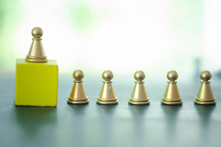 The golden pawn chess piece standing out of the group and on a yellow wood block, stand out from the crowd. Leadership, unique, influencer, boss concept.の写真素材