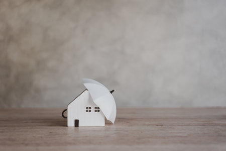 Small umbrella and house figure. Umbrella protect to home. Loan or saving money for property protection real estate concept.の写真素材