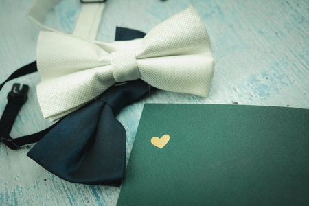 Green bow tie and white bow tie with green notebook with golden heart logo, top view. Flat lay of rustic wedding invitationの写真素材