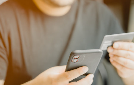 Close up male client holding card and smartphone in hands, making payments using mobile application, shopping online in internet store, purchasing goods or services. Shopping online order deliveryの写真素材