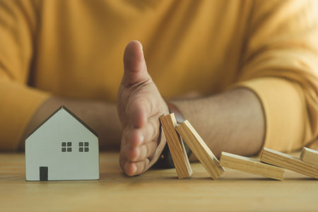 Businessman hand gesture protects falling domino to the house for insurance and insurance concept. Life safety financial stability. Real estate house insurance. Domino chain challenge and protectionの写真素材