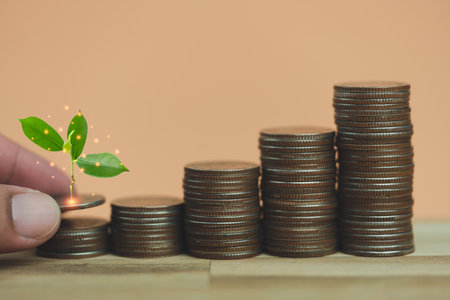 Man hand holding coin with tree growing putting on money coin stack arranged as a graph on wooden table, concept of money growth and saving moneyの写真素材