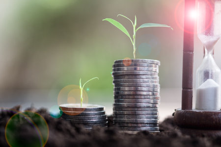 Plants are grown on a pile of coins and sandglass for finance and banking. The idea of saving money...