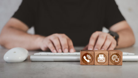 Man using a keyboard with contact icons on wood block. Cell phone, address, and website. Customer support hotline and contact us people connection. Customer support conceptの写真素材