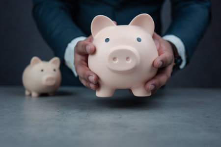 Businessman holding large piggy bank with small piggy bank placed on the table. Business finance and investment concept. Finance Savings concept. A businessman in suit is holding piggy bank.の写真素材