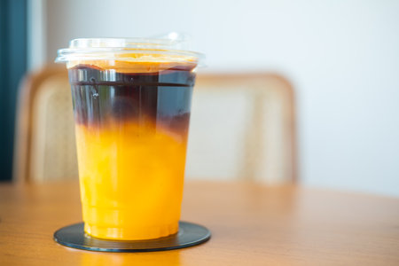 A glass of iced Americano black coffee and a layer of orange juice on the wood backgroundの写真素材