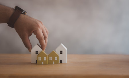Man choosing mini wood house model from the model on wood table, Planning to buy property. Concept of choosing the best. Real estate concept.の写真素材