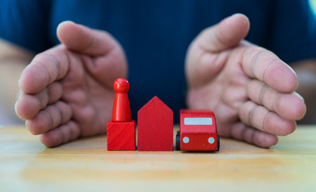 Man showing a red car figure model and red home with red wooden human model on the table. Concept of insurance with hands over a houseの写真素材