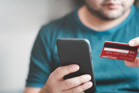 Man wear blue green t-shirt use mobile cell phone credit bank card shopping online order delivery at home. Makes purchase onlineの写真素材