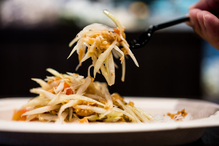 Somtum Thai green papaya salad tastes spicy sour and sweet on black forkの写真素材