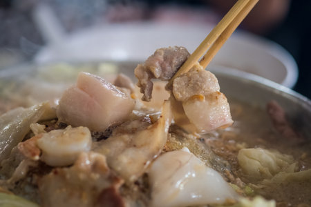 Hand uses chopsticks to pick up pork to be grilled in a  hot pan. Thai barbecue Grill Pork on hot pan buffet, It traditional Thai style BBQの写真素材