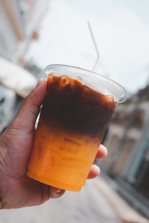 A glass of iced americano black coffee and layer of orange juice in hand.
