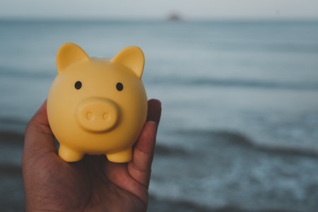 Hand holding cute yellow piggy bank against on the sea background. Saving planning for Travel budget of holiday conceptの写真素材