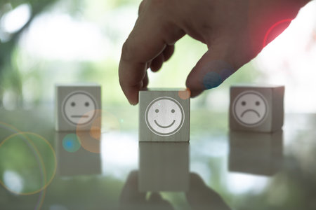 Male hand chooses the happy face among unhappy faces on wooden blocks. Customer service evaluation and satisfaction survey service rating conceptの写真素材