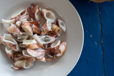 Grilled squid. Grilled squid, cut into bite-sized pieces. Served in a white plate on a wooden table.の写真素材