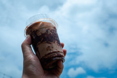 Hand holding iced mocha with showing the texture and refreshing look of the drink on blue sky backgroundの写真素材