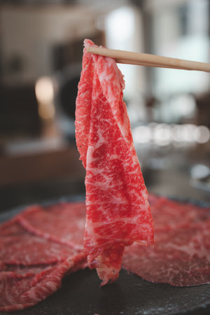 Premium rare slices beef with high marbling texture pick up by wood chopsticks with hand from stone...