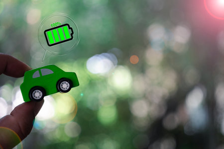 Man hand holding wood green car with full battery icon with copy space on nature green background. Energy car concept.の写真素材