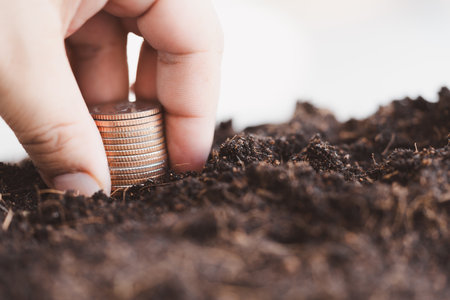 Man hand keeps of a stack of coins from the soil. Money growth and dividend interest, planning...