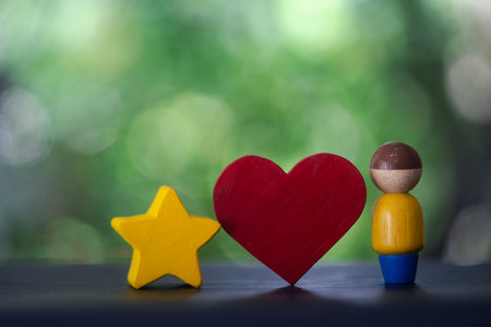 Wooden human figure dolls with red heart shape and yellow star shape against nature background.の写真素材