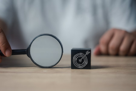 Target board icon in wood block and man use magnifier glass for focus business objective achievement. The concept of search, goal, strategy and success.の写真素材