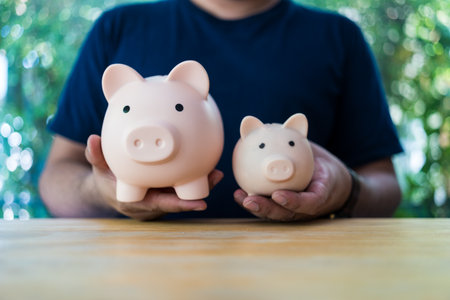 A young man holding with small pink pig moneybox and a big pink pig money box for different objectives saving. The concept of saving moneyの写真素材