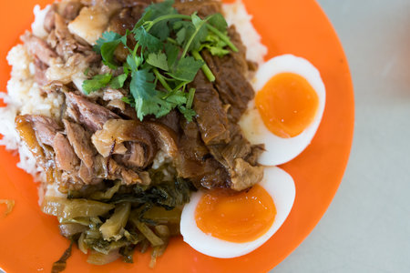 Thai pork leg pot stewed with rice and boiled egg on a orange dish. Street food Thai.の写真素材