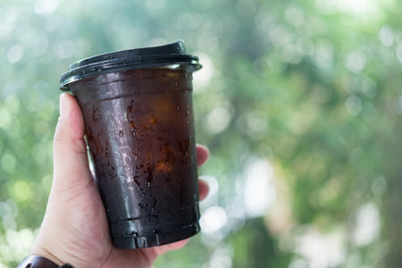 Hand holding iced black coffee or americano coffee in takeaway glassの写真素材