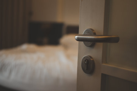 Close up of a lock door handle in a luxury resort hotel and a wood panelled contemporary door, background of bed and pillows in the roomの写真素材