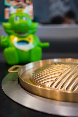 Bangkok, Thailand - December 5, 2023: Brass pan placed on the electric stove on the table with mascot "Bar-B-Gon" at Bar B Q Plaza restaurant, is a famous barbeque restaurant in Thailandのeditorial素材
