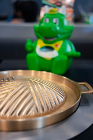 Bangkok, Thailand - December 7, 2023: Brass pan placed on the electric stove on the table with mascot "Bar-B-Gon" at Bar B Q Plaza restaurant, is a famous barbeque restaurant in Thailandのeditorial素材
